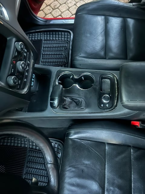 Vehicle interior showing black leather seats, steering wheel, center console with cup holders and controls, and dashboard