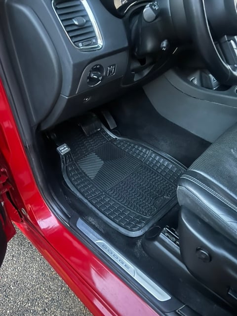 Interior view of red car showing black rubber floor mats, steering wheel, and dashboard controls