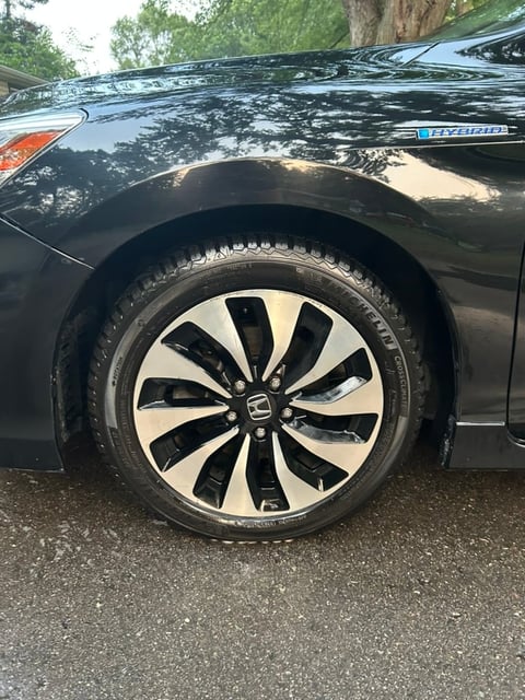 Close-up of a black Honda vehicles wheel with two-tone alloy rim, parked with trees in the background