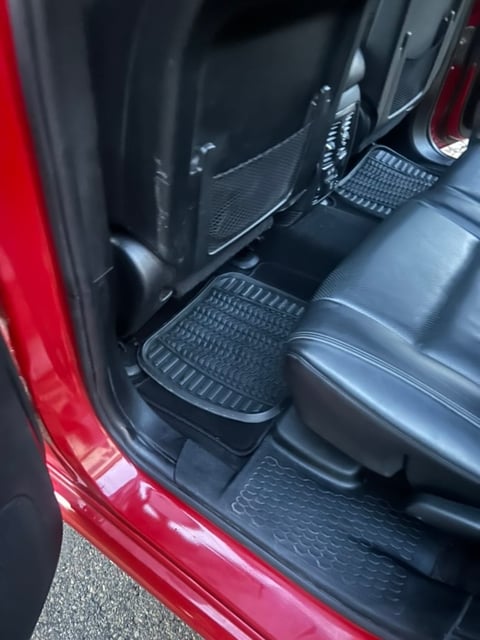 Interior of red vehicle showing front seats and black rubber floor mats with textured pattern