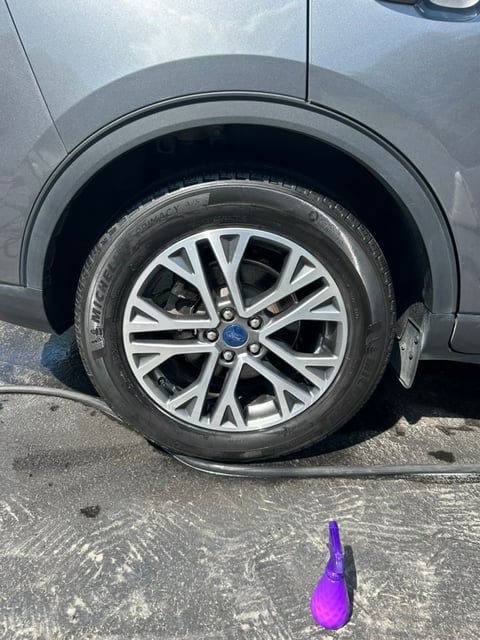 Close-up of a silver car wheel with alloy rim and tire on asphalt, with a purple object in foreground