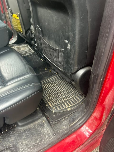 Dirty red truck interior showing passenger seat, rubber floor mats, and door panels with visible dust and grime