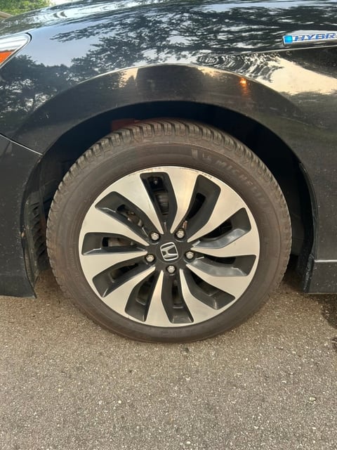 Close-up of a dark car wheel with two-tone white and black alloy rim and tire on asphalt surface
