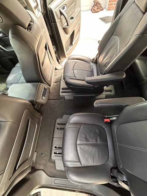 Interior view of vehicle showing black leather seats with gray stitching and center console, doors open to bright daylight