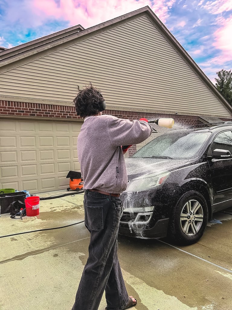 Person in purple hoodie washing a black car in a driveway