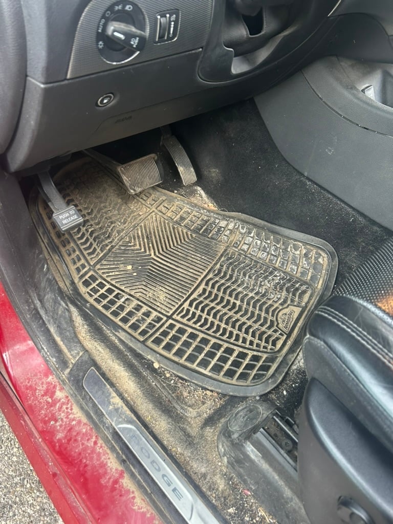 Close-up of car interior showing dirty rubber floor mats with geometric patterns on the driver side footwell