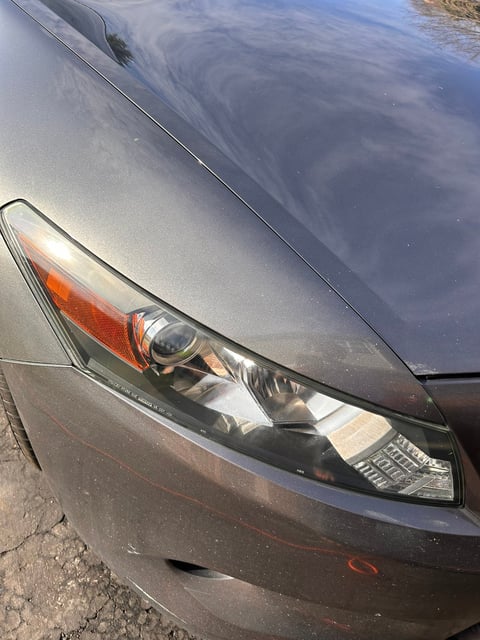 Close-up of a gray cars headlight and front fender showing the headlamp detail and hood reflection