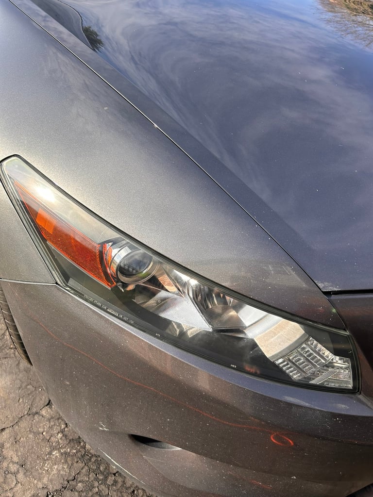 Close-up of a gray cars headlight and front fender showing the headlamp detail and hood reflection